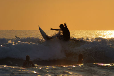 People on sea against sky during sunset