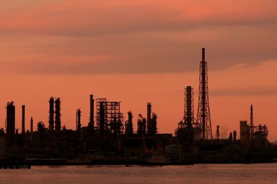 Cranes by sea against sky during sunset