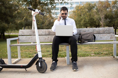 Full length of businessman using laptop sitting on bench in park