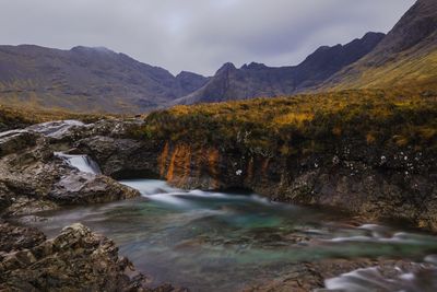Scenic view of waterfall by mountains against sky