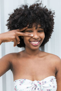 Smiling young woman doing peace gesture in front of wall