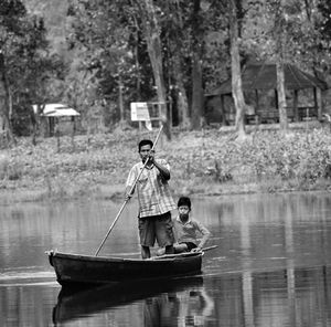 Boy sitting on boat in lake against trees