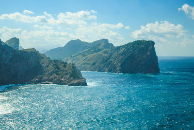 Scenic view of sea by mountain against sky