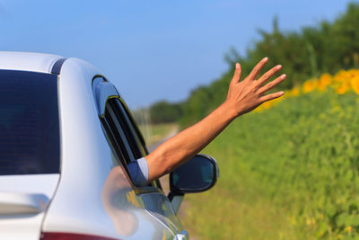 Cropped hand gesturing from car against clear blue sky