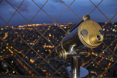 Coin-operated binoculars overlooking cityscape seen through chainlink fence