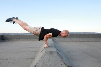 Full length of man exercising on building terrace against the sky