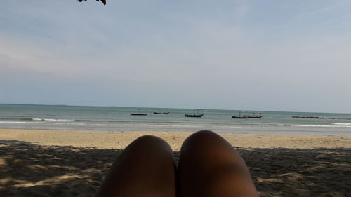 Low section of woman relaxing on beach against sky