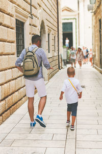 Rear view of father and son while walking walking on the street.