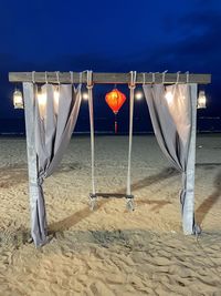 Illuminated lighting equipment hanging on beach against sky at night