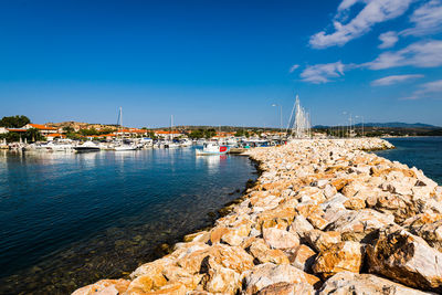 Sailboats on rock by sea against blue sky