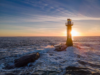 Lighthouse by sea against sky during sunset