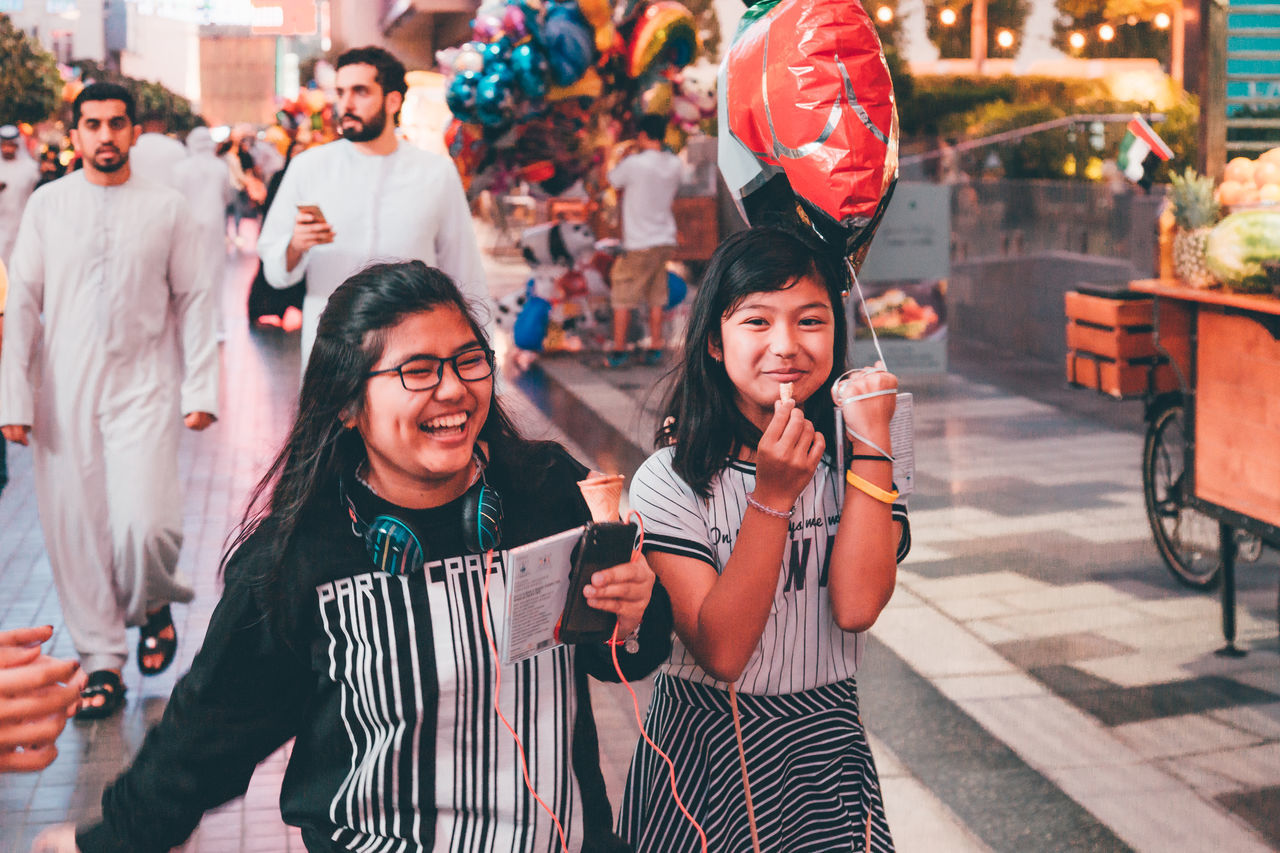 celebration, real people, young women, smiling, two people, young adult, happiness, lifestyles, holiday - event, outdoors, togetherness, leisure activity, standing, cheerful, day, women, building exterior, friendship, portrait, city