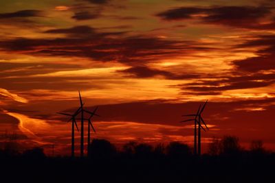 Silhouette wind turbines on field against orange sky