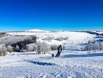 Rear view of woman skiing on snow covered field against clear blue sky