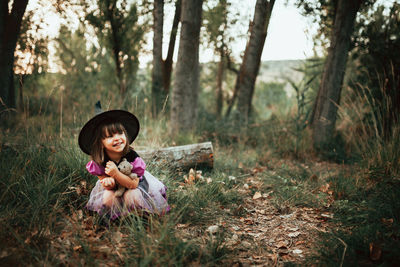 Girl holding toy while sitting on land in forest