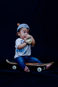 Cute boy looking away while standing against black background