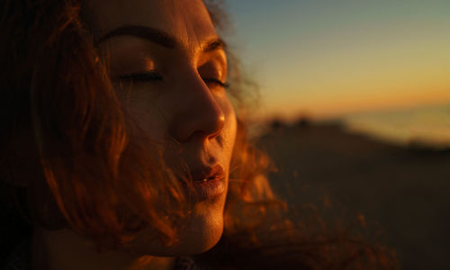 Close-up of woman with closed eyes standing outdoors during sunset