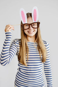 A teenage girl in a mask-glasses with rabbit ears in a striped sweater on a light background 