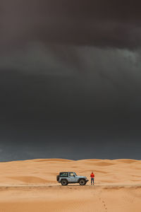 Dark storms clouds and rain over sand dunes and jeep in utah desert