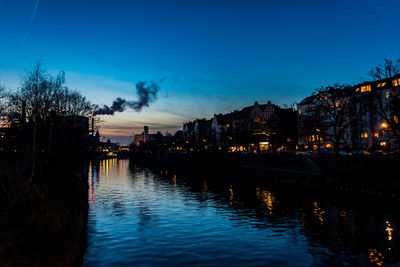 River by illuminated buildings against blue sky at night