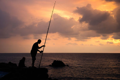 Silhouette man fishing in sea against sunset sky