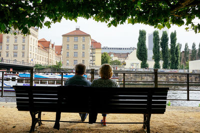 Rear view of couple sitting against buildings in city