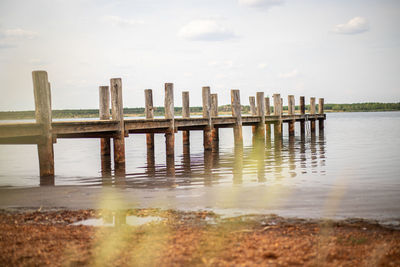 Wooden posts on pier over lake against sky