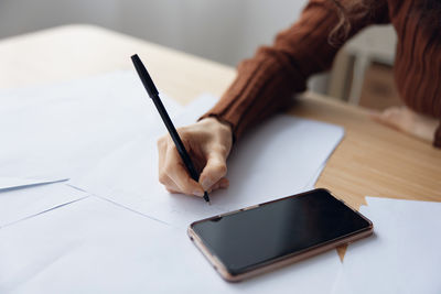 Midsection of woman writing in book on table