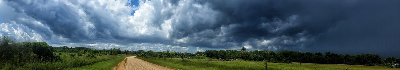 Road passing through field against cloudy sky