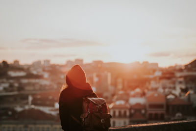 Rear view of woman standing against cityscape during sunset