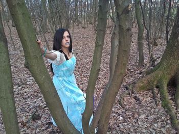 Portrait of young woman standing on tree trunk in forest