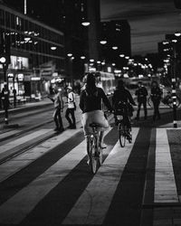 Rear view of people riding bicycle on road at night