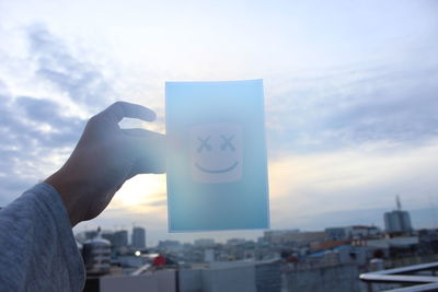 Midsection of man holding cityscape against sky during sunset