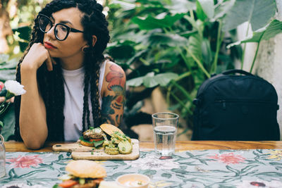 Young woman looking away while sitting by food on table at restaurant