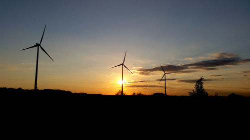 Silhouette of wind turbines on field against sky during sunset