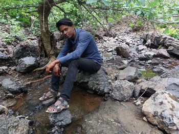 Full length of woman sitting on rock in forest