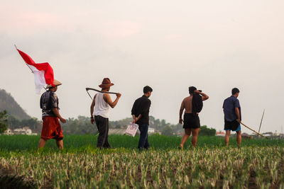 Rear view of people standing on field against sky