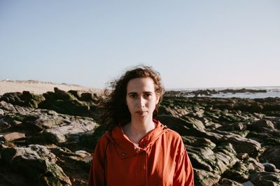 Portrait of young woman standing on rock against clear sky