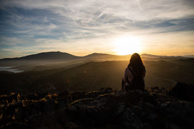 Rear view of woman standing on mountain against sky during sunset