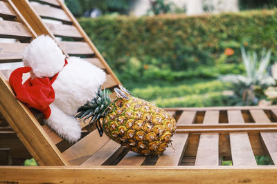 Side view of relaxing funny pineapple wearing sunglasses and santa claus hat lies on wooden sunbed