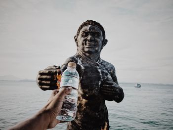 Statue of man holding sculpture against sea