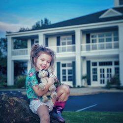 Portrait of girl sitting with stuffed toy on rock