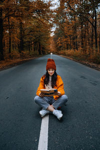 Confidence woman with book sitting on the road with autumn tree around. new life, path choice