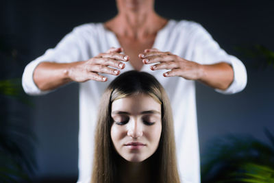 Midsection of therapist giving reiki treatment to teenage girl on head at spa