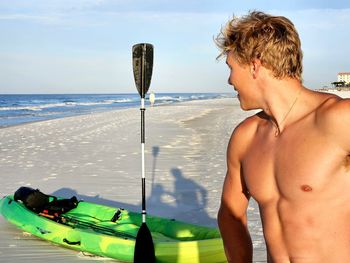 Rear view of shirtless man in boat in sea against sky