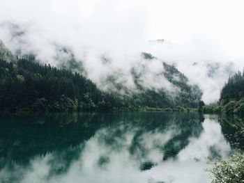 Scenic view of lake by mountains during foggy weather