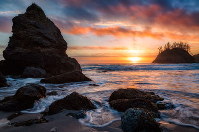 Rocks on beach against sky during sunset