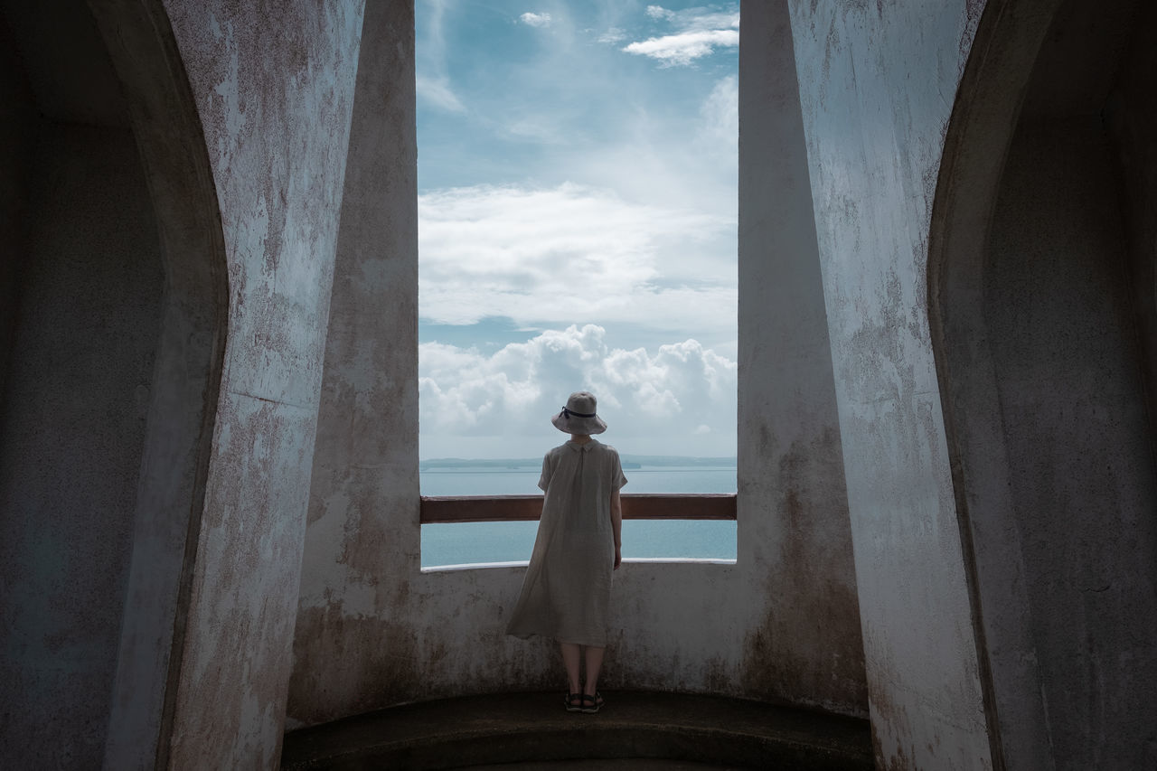 one person, standing, real people, architecture, lifestyles, built structure, full length, leisure activity, sky, rear view, cloud - sky, day, nature, indoors, men, adult, window, women, looking at view, contemplation