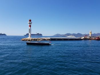 Lighthouse by sea against clear blue sky