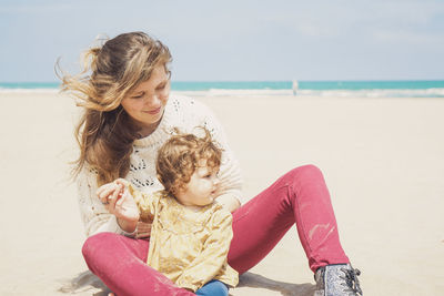 Happy woman sitting on shore at beach against sky